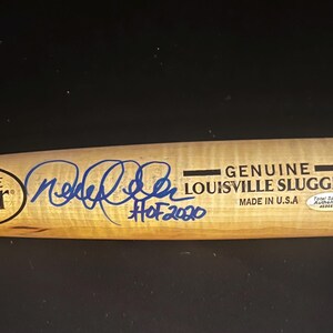 Pode incluir: Um taco de beisebol de madeira clara da marca Louisville Slugger com uma assinatura em tinta azul e o texto HOF 2020. O taco inclui o logótipo Louisville Slugger, o texto Genuine Louisville Slugger Made in U.S.A. e um autocolante Total Sports Authentics.