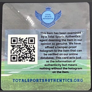 May include: A square authentication card featuring a Total Sports Authentics logo with wings and a crown, a QR code, and text stating the item has been examined and deemed genuine. The background shows a blurred stadium field, with the website URL at the bottom.