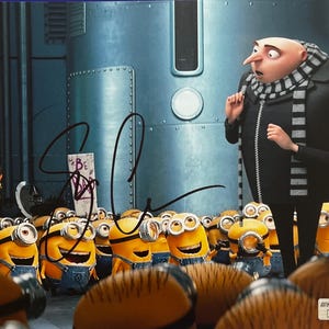 Op de afbeelding: Een gesigneerde filmafdruk met Gru in een zwart jasje en gestreepte sjaal voor een menigte gele Minions. Een bord op de achtergrond leest Follow Mel, en een ander bord zegt Be Bad. Een authenticatiesticker bevindt zich in de hoek.