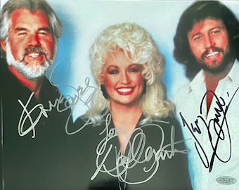 May include: A color photograph featuring three individuals with signatures overlaid on the image. The left figure has a white beard and black shirt, the center figure has blonde hair and a black top, and the right figure has a beard and white shirt.