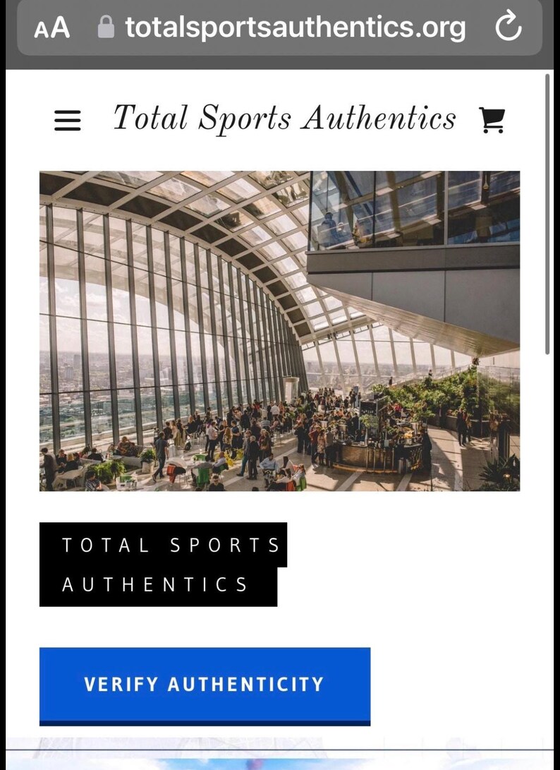 Może przedstawiać: Zrzut ekranu strony internetowej Total Sports Authentics. Obraz przedstawia duży, nowoczesny budynek ze szklanym dachem i wieloma ludźmi. Wyświetlany jest tekst "Total Sports Authentics" wraz z przyciskiem "Zweryfikuj autentyczność".