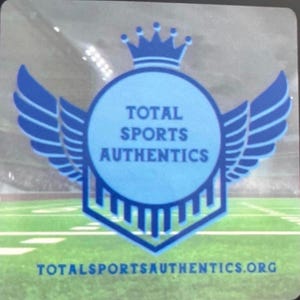 May include: A square sticker featuring a blue circular emblem with a crown on top and wings on the sides. The text TOTAL SPORTS AUTHENTICS is centered in the circle, and the website TOTALSPORTSAUTHENTICS.ORG is printed in blue at the bottom.