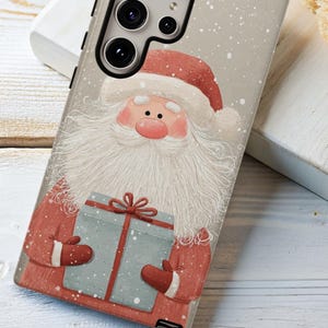 May include: A phone case featuring a festive Santa Claus design. The case has a light beige background with a watercolor illustration of Santa holding a blue gift box. Santa is wearing a red suit and hat with a white beard. Snowflakes are falling in the background.
