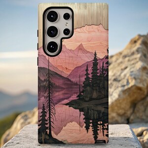 May include: A wooden phone case featuring a landscape design with mountains, trees, and a lake. The artwork uses shades of pink, purple, and black. The phone case has a camera module with multiple lenses.