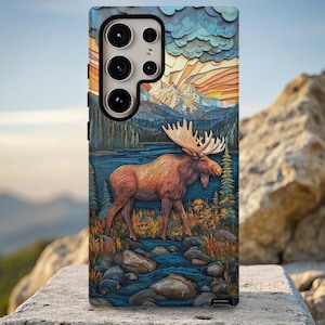 May include: A phone case featuring a detailed illustration of a moose in a natural landscape. The design includes a moose walking near a river, with mountains and a colorful sky in the background. The case has a textured appearance.
