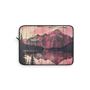May include: Laptop sleeve with a mountain landscape design. The artwork shows a mountain range reflected in a lake, with pink and purple hues. The sleeve has a black border and a zip.