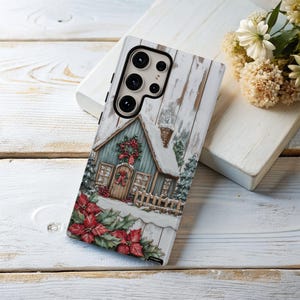 May include: A phone case featuring a winter scene with a snow-covered house, a wreath, and red poinsettias. The case has a textured, weathered wood background. The phone case is designed to fit a smartphone.