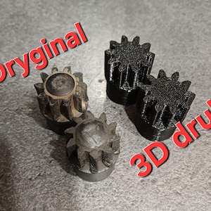 Op de afbeelding: Vier tandwielvormige objecten, twee in zwart en twee in metallic grijs. De tekst "Oryginal" en "3D druk" staan in het rood, schuin over de afbeelding. De tandwielen hebben een centraal cirkelvormig kenmerk en getande randen.