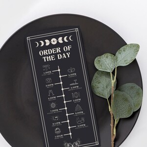 Puede incluir: Una tarjeta negra con un borde blanco y un diseño de luna y estrella. La tarjeta enumera el orden del día para una boda, incluyendo las horas de llegada de los invitados, la ceremonia, las fotos, las bebidas y los canapés, la cena, la recepción de la noche, el primer baile y el buffet de la noche.