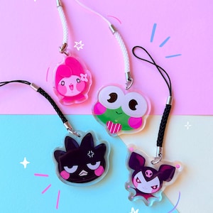 Può includere: Quattro ciondoli in acrilico trasparente con disegni di personaggi, ciascuno attaccato a un cordino. I personaggi includono una ragazza rosa, una rana verde, un uccello nero e un pipistrello viola. Lo sfondo è diviso tra rosa e blu.