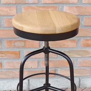 Pode incluir: Um banquinho de bar de metal preto ajustável em altura com um assento redondo de madeira.