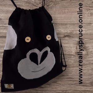 May include: Black drawstring bag with a white and grey monkey face design. The bag has two wooden buttons for eyes.