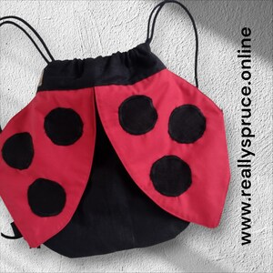 May include: A drawstring backpack designed to resemble a ladybird, featuring a black base with red fabric wings adorned with black circular spots. The bag includes black cord straps and the text www.reallyspruce.online printed vertically.