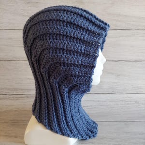 May include: A blue crocheted hood, shown on a white mannequin head. The hood has a ribbed pattern and covers the head and neck. The yarn is a solid, medium blue colour.