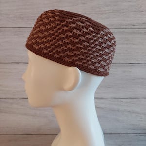 May include: A brown and beige crocheted hat with a geometric pattern. The hat is worn on a white mannequin head.