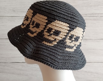 May include: A black and beige crocheted bucket hat with a skull pattern. The hat is on a white mannequin head.
