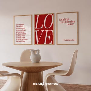 May include: Three framed art prints with inspirational quotes. The central print features the word "LOVE" in bold red letters. The other two prints display quotes about love in red text. A wooden table and chairs are in the foreground.