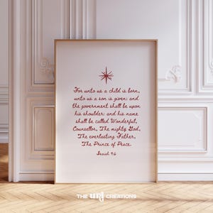 May include: Framed print with a gold border featuring red text and a starburst design. The text reads "For unto us a child is born...Isaiah 9:6." The print is displayed against a white wall and wooden floor.
