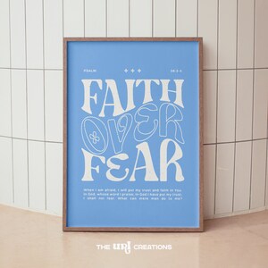 May include: A blue poster with white text that reads "FAITH OVER FEAR" in a stylized font. The poster also includes a Bible verse from Psalm 56:3-4, which reads "When I am afraid, I will put my trust and faith in You. In God, whose word I praise, In God I have put my trust, I shall not fear. What can mere man do to me?" The poster is framed in a light brown wood frame.