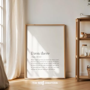 May include: A framed print with a white background and black text. The text reads "Even there / Psalm 139:7-10 / Where could I go from your Spirit? Or where could I flee from your presence? If I ascend up into heaven, you are there. If I make my bed in Sheol, behold, you are there! If I take the wings of the dawn, and settle in the uttermost parts of the sea, even there your hand will lead me, and your right hand will hold me." The print is sitting on a wooden floor.