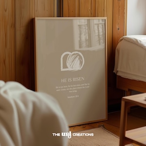 May include: A beige printable wall art print with a white graphic of a stone tomb with the words "He is Risen" and a Bible verse from Matthew 28:6.
