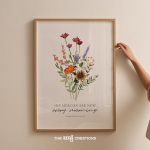 May include: A framed floral art print with a watercolour bouquet of red, orange, purple, and yellow flowers. The print includes the text "HIS MERCIES ARE NEW every morning" and "LAMENTATIONS 3:22-23". The bottom of the frame has the text "THE URI CREATIONS".