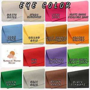 May include: A grid of sixteen felt fabric swatches labeled EYE COLOR, displaying white, ivory, pink, dusty rose, blue, yellow, rust orange, orange, red, lavender, grass green, green, gray, brown, and black, with a Natural Home Decor logo.