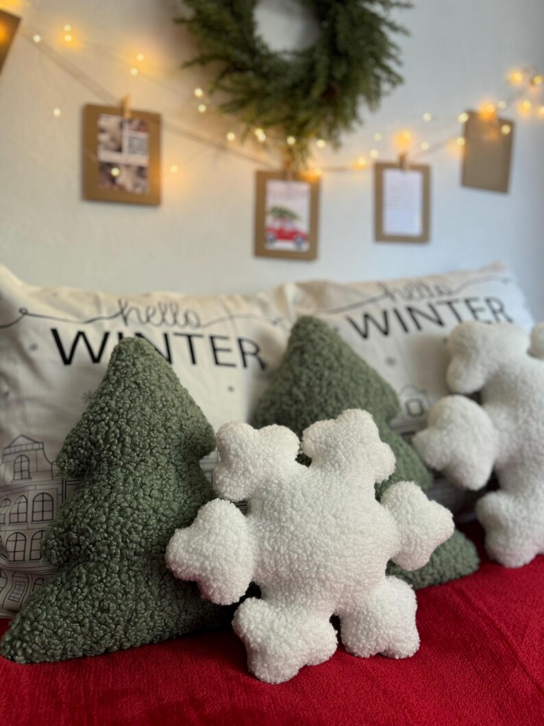 May include: Three plush pillows with winter-themed designs. A green tree-shaped pillow, a white snowflake-shaped pillow, and a white pillow with the text "hello winter" in black.
