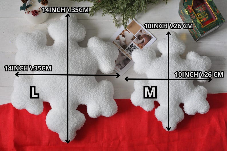 May include: Two white plush snowflake pillows, one large and one medium. The large pillow measures 14 inches by 14 inches, and the medium pillow measures 10 inches by 10 inches. Both pillows are made of soft, fluffy material.