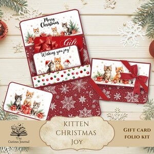 May include: A Christmas gift card folio kit featuring illustrations of kittens. The kit includes multiple cards with red bows and the phrases "Merry Christmas" and "Wishing you joy!". The background is a festive red with snowflake patterns.