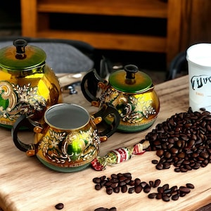 Può includere: Un set di tre teiere dorate e verdi con intricati disegni floreali, una tazza bianca con la scritta "True" e un mucchio di chicchi di caffè su una superficie di legno.