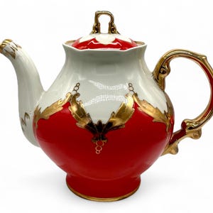 May include: A red and white porcelain teapot with gold accents and a floral design. The teapot has a round body and a curved spout. The handle is gold and has a decorative design.