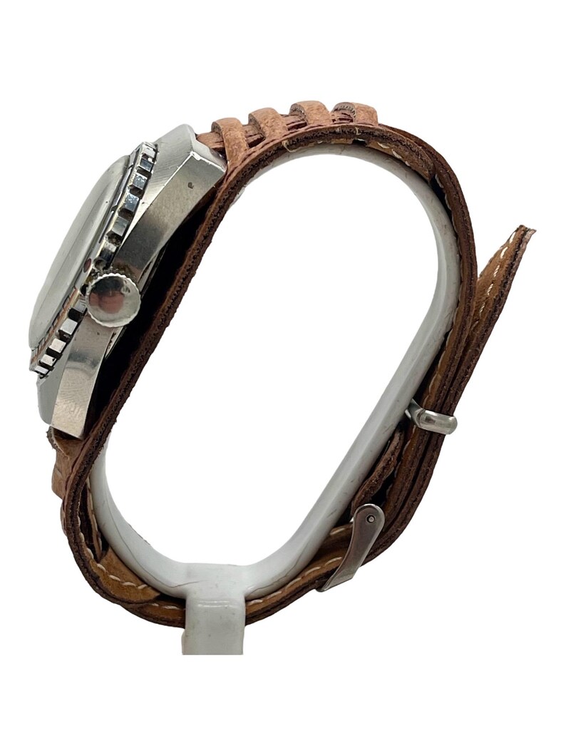 Puede incluir: Un reloj de pulsera plateado con una correa de cuero marr&oacute;n. El reloj tiene una esfera redonda con un bisel negro y una corona plateada.