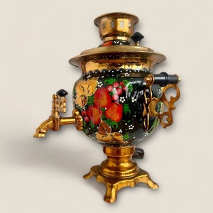 May include: A traditional Russian samovar with a black and gold painted design featuring red and green floral motifs. The samovar has a brass spout and handle, and a gold base with four legs.