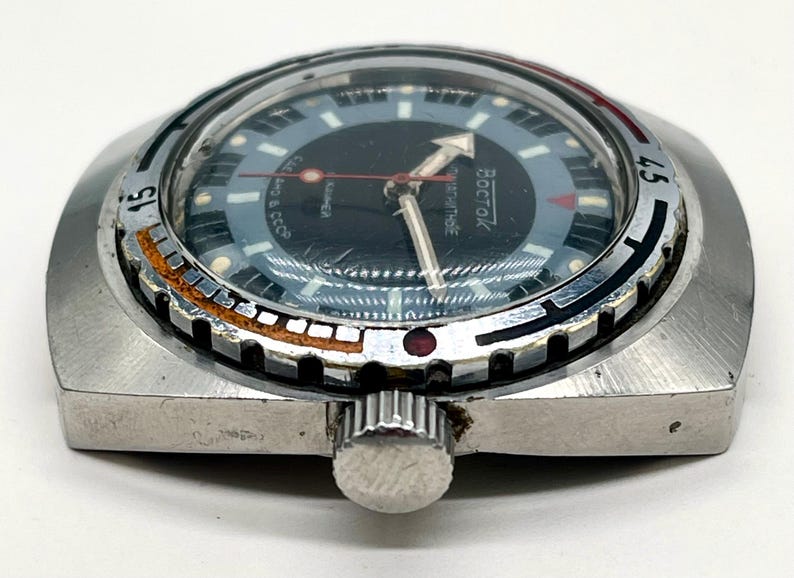 Puede incluir: Un reloj de pulsera plateado con una esfera negra y una aguja de segundos roja. El reloj tiene un bisel giratorio con marcas negras y blancas y la palabra "BOCTAK" impresa en la esfera.