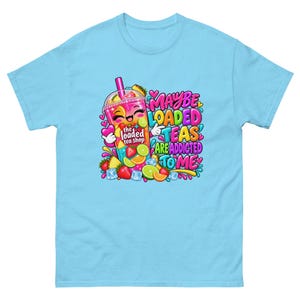 Puede incluir: Una camiseta azul claro con un gráfico colorido de un vaso de té helado antropomórfico sonriente rodeado de fresas, rodajas de lima y cubitos de hielo. El texto dice "MAYBE LOADED TEAS ARE ADDICTED TO ME" y "the loaded tea shop".