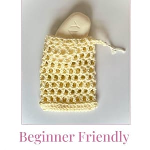May include: A crocheted soap saver in a pale yellow colour, with a bar of soap inside. The soap saver is a beginner-friendly crochet pattern. The text "Crochet Soap Saver Pattern" is at the top of the image, and "Beginner Friendly" is at the bottom.