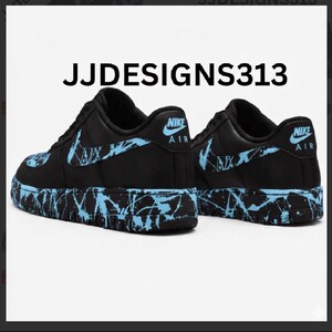 May include: Pair of black Nike Air Force 1 sneakers with light blue splatter paint design on the soles and swoosh logos. The text "JJDESIGNS313" is printed above the shoes.