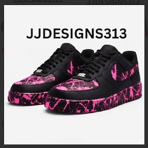 May include: Pair of black sneakers with pink splatter paint design on the toe, side, and sole. The Nike swoosh is pink. The text "JJDESIGNS313" is printed in white on the top of the image.