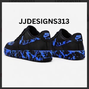 May include: Pair of black Nike Air Force 1 sneakers with blue splatter paint design on the soles, swoosh, and heel. The text "JJDESIGNS313" is above the shoes.