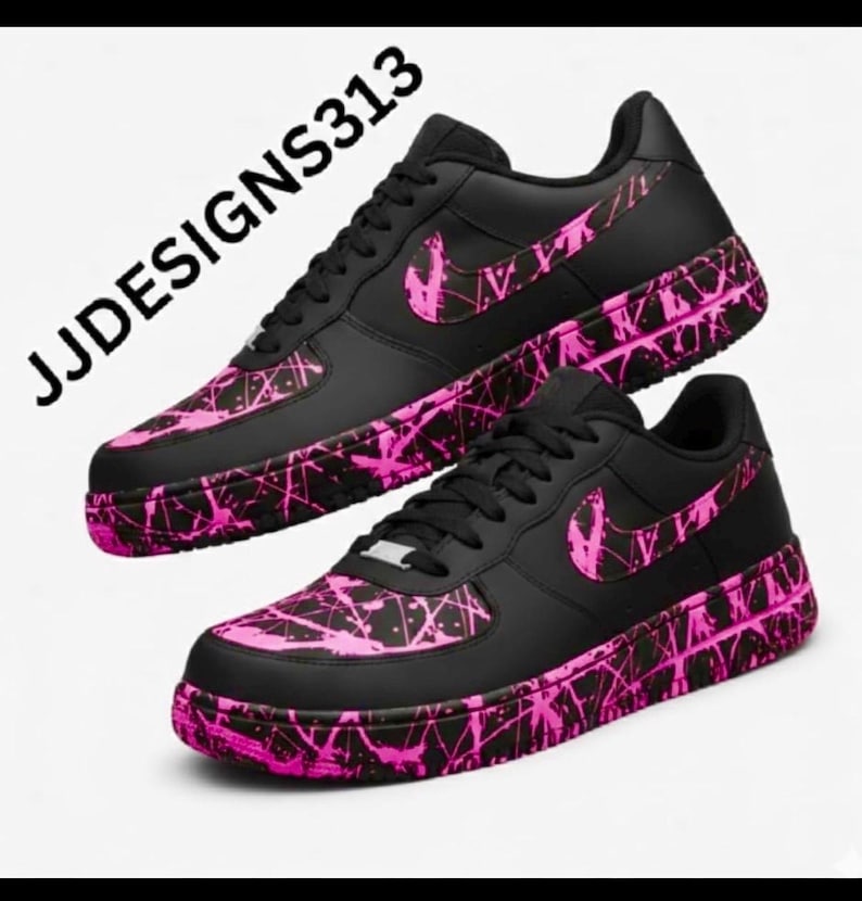 May include: Pair of black sneakers with pink splatter design accents. The shoes feature a pink Nike swoosh and a pink splatter pattern on the toe and sole. The text "JJDESSIGNS313" is visible.
