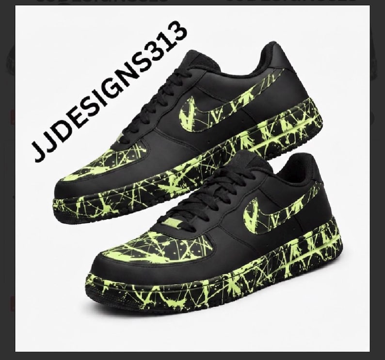 May include: Black sneakers with neon green splatter paint design. The Nike swoosh is also neon green. The text "JJDESIGNS313" is in the upper left corner. The shoes are on a white background.