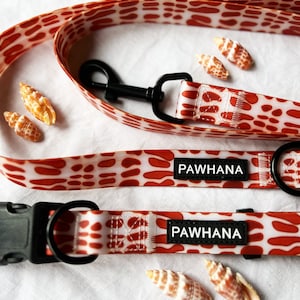 May include: A red and white patterned dog leash and collar set with black hardware and the text "PAWHANA" on the leash and collar.