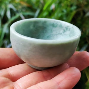Op de afbeelding: Een kleine, lichtgroene jadeschaal met een glad, gepolijst oppervlak. De schaal is ongeveer 5 cm in diameter en 2,5 cm hoog.