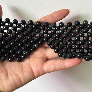 May include: A rectangular eye mask constructed from a grid of small, polished, dark green spherical beads. The beads are arranged in a uniform pattern, connected by thin, flexible material, creating a semi-flexible, lightweight structure.