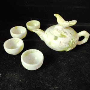 Puede incluir: Una taza de cerámica blanca con un asa negra y el texto "But First, Coffee" en un estilo manuscrito. La taza está sobre una superficie blanca. La taza mide aproximadamente 10 cm de alto.