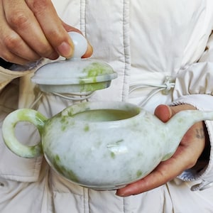 Puede incluir: Una tetera de mármol blanco y verde con tapa a juego. La tetera tiene un cuerpo redondeado, un asa curva y un pico. La tapa se levanta, revelando el interior. El mármol tiene un patrón natural moteado.