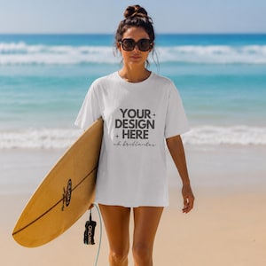 May include: A white short-sleeve t-shirt featuring the dark gray text YOUR DESIGN HERE with small star icons and the cursive script ch brillantes printed on the front. The shirt has a crew neckline and a relaxed fit, shown in a beach setting.