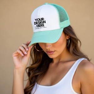 Puede incluir: Una gorra de camionero blanca y verde claro con una malla en la parte posterior. La parte delantera de la gorra tiene texto negro que dice "YOUR DESIGN HERE + oh.brilliance".