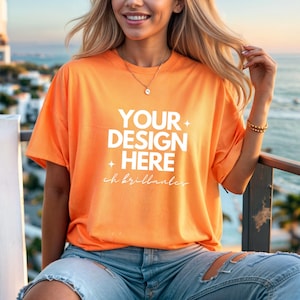 Puede incluir: Una mujer lleva una camiseta naranja brillante con el texto "YOUR DESIGN HERE" y las palabras "ch brilliantes" debajo. Lleva pantalones vaqueros azules y tiene el pelo recogido hacia atrás.